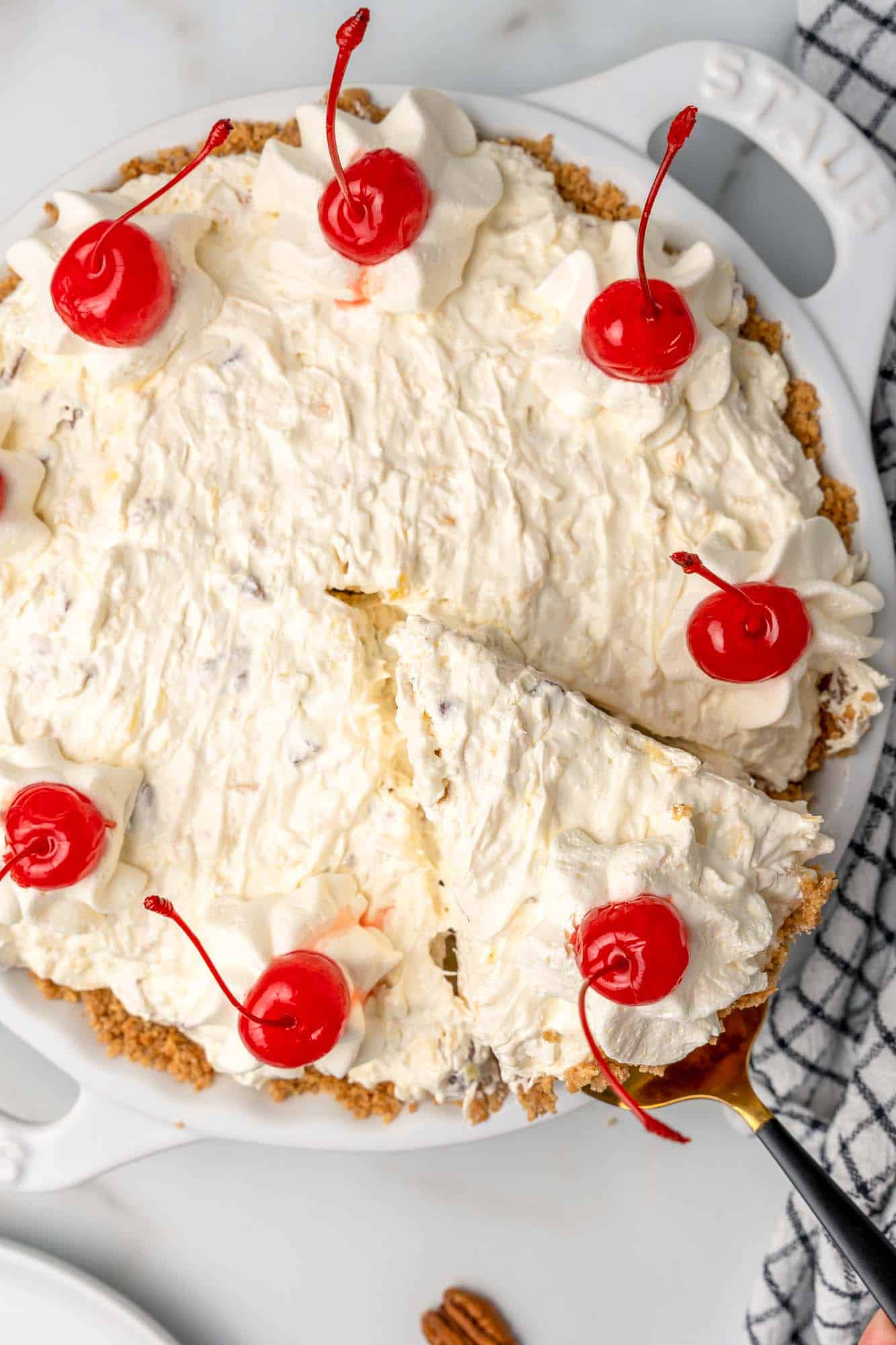 creamy million dollar pie topped with cherries, viewed from above. A slice is being lifted out. 