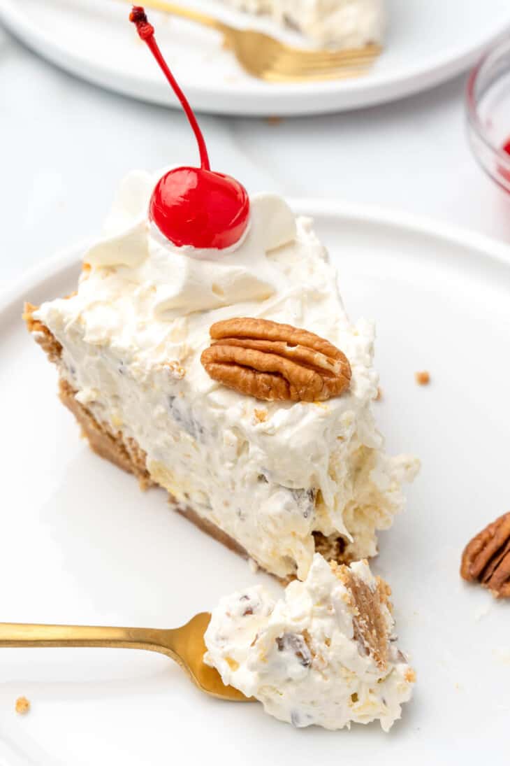 A slice of creamy pie topped with whipped cream, a maraschino cherry, and a pecan sits on a white plate with a gold fork—perfect inspiration for easy pie recipes or celebrating National Pie Day.