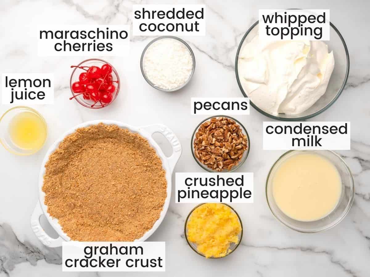 The ingredients for million dollar pie, including a prepared graham cracker crust and whipped topping, all measured out in separate bowls, viewed from above