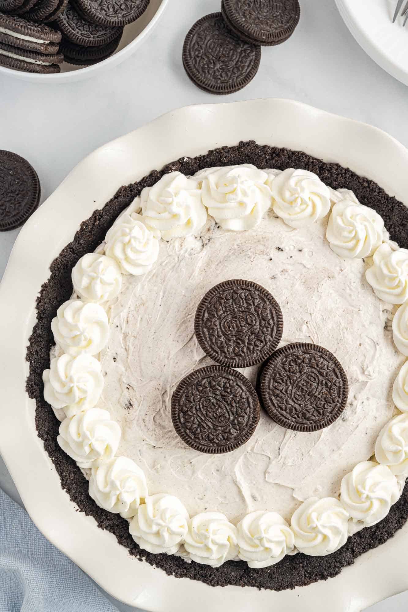 A whole oreo pie in a white pie plate, topped with whipped cream and oreo cookies, viewed from above.