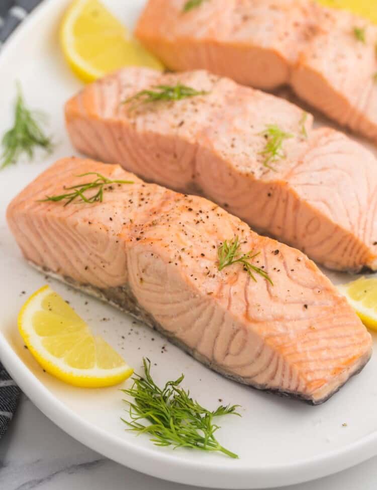 3 poached salmon fillets served on a white oval platter, with slices of lemon and fresh dill.