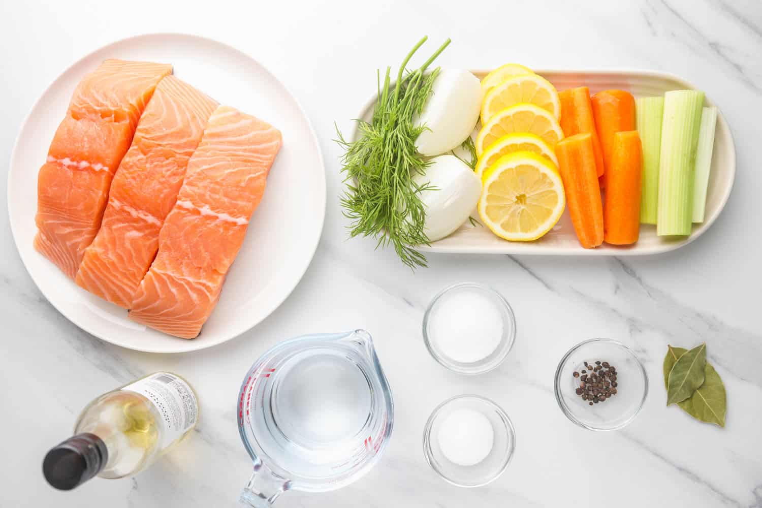 Ingredients needed to poach salmon including salmon fillets, lemon, onion, celery, carrot, dill, bay leaf, white wine, water, salt, sugar, peppercorns.
