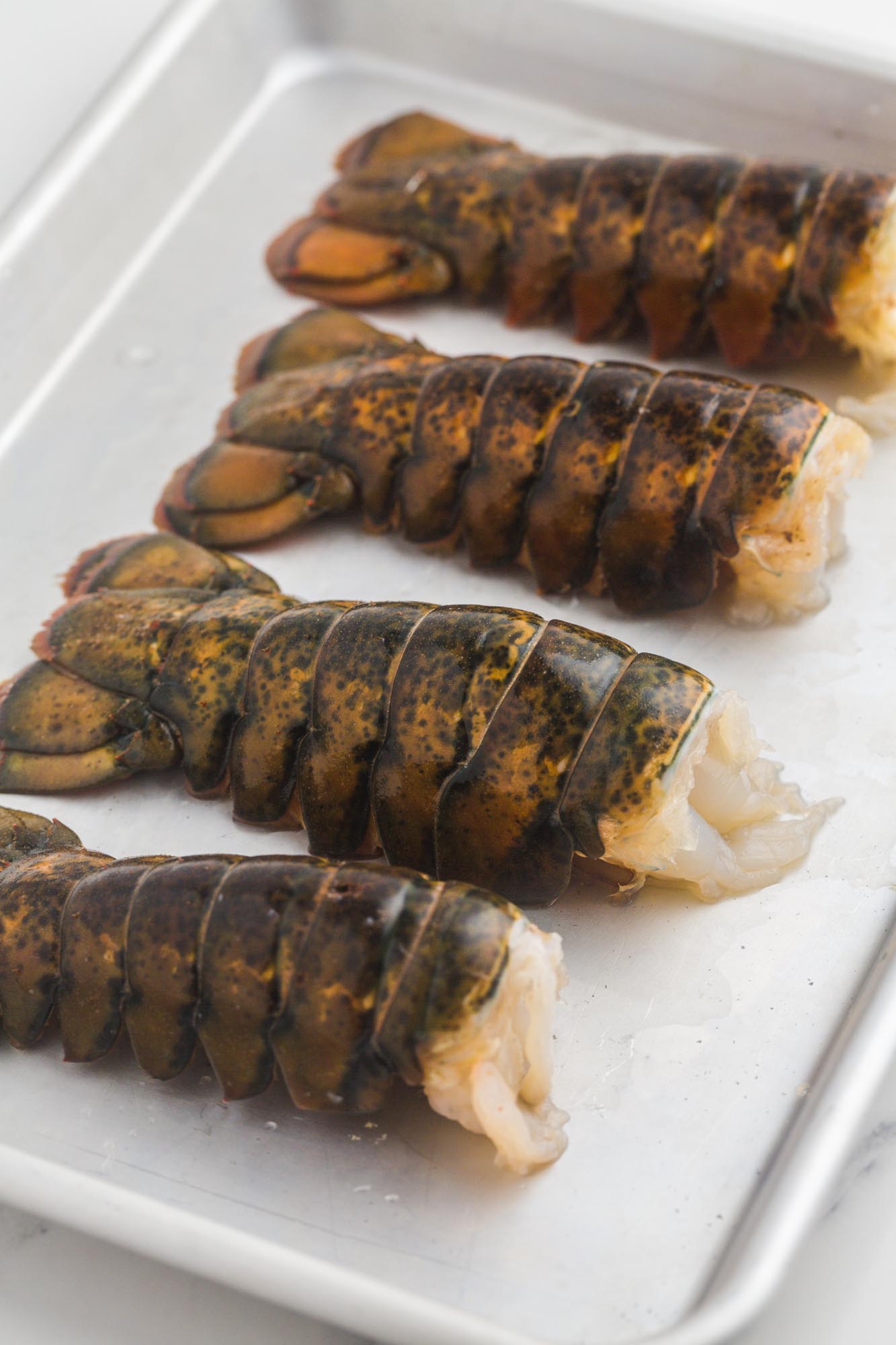 4 raw and thawed lobster tails placed on a sheet pan