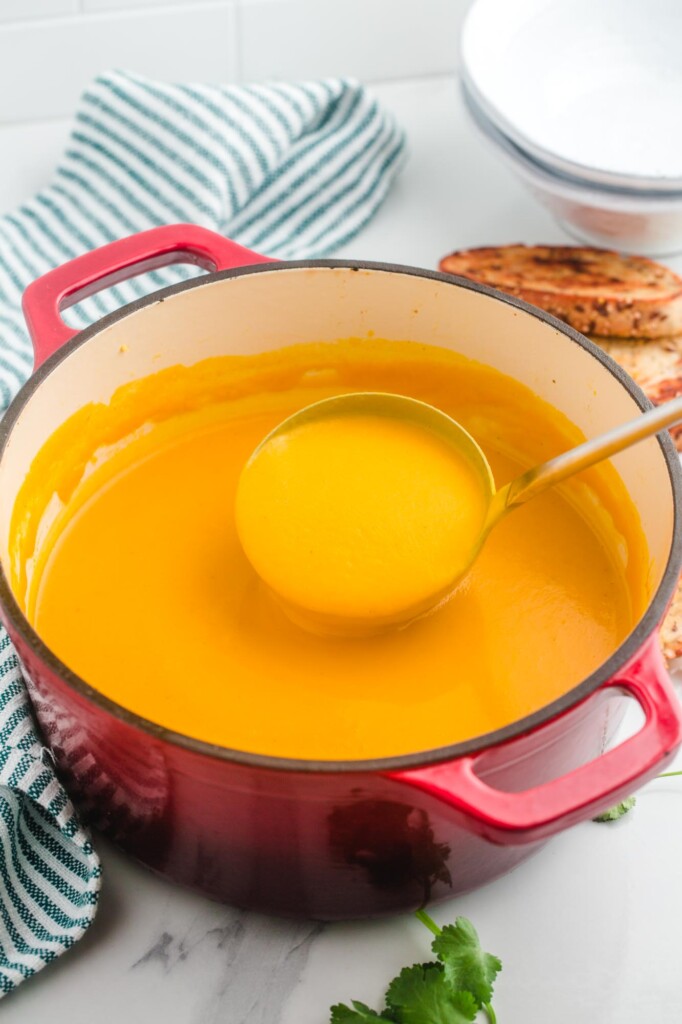 Sweet Potato soup in a large red dutch oven and a soup ladle