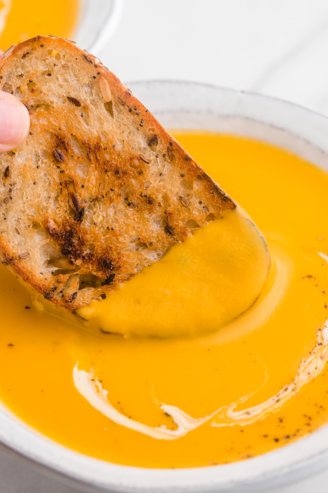 Dipping toasted bread in sweet potato soup, close up shot.