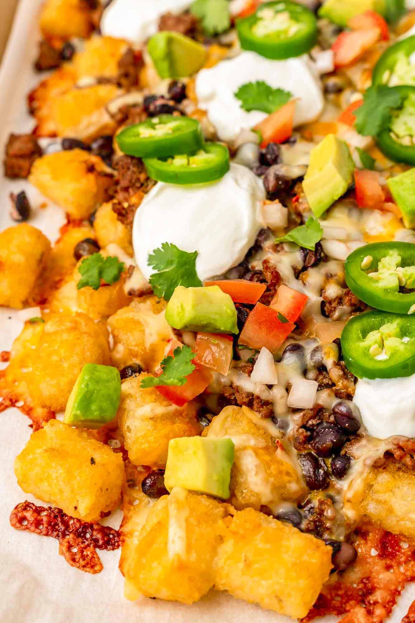 Close up shot of tater tot nachos with ground beef and beans, topped with sour cream, jalapeno, avocado, and pico de gallo