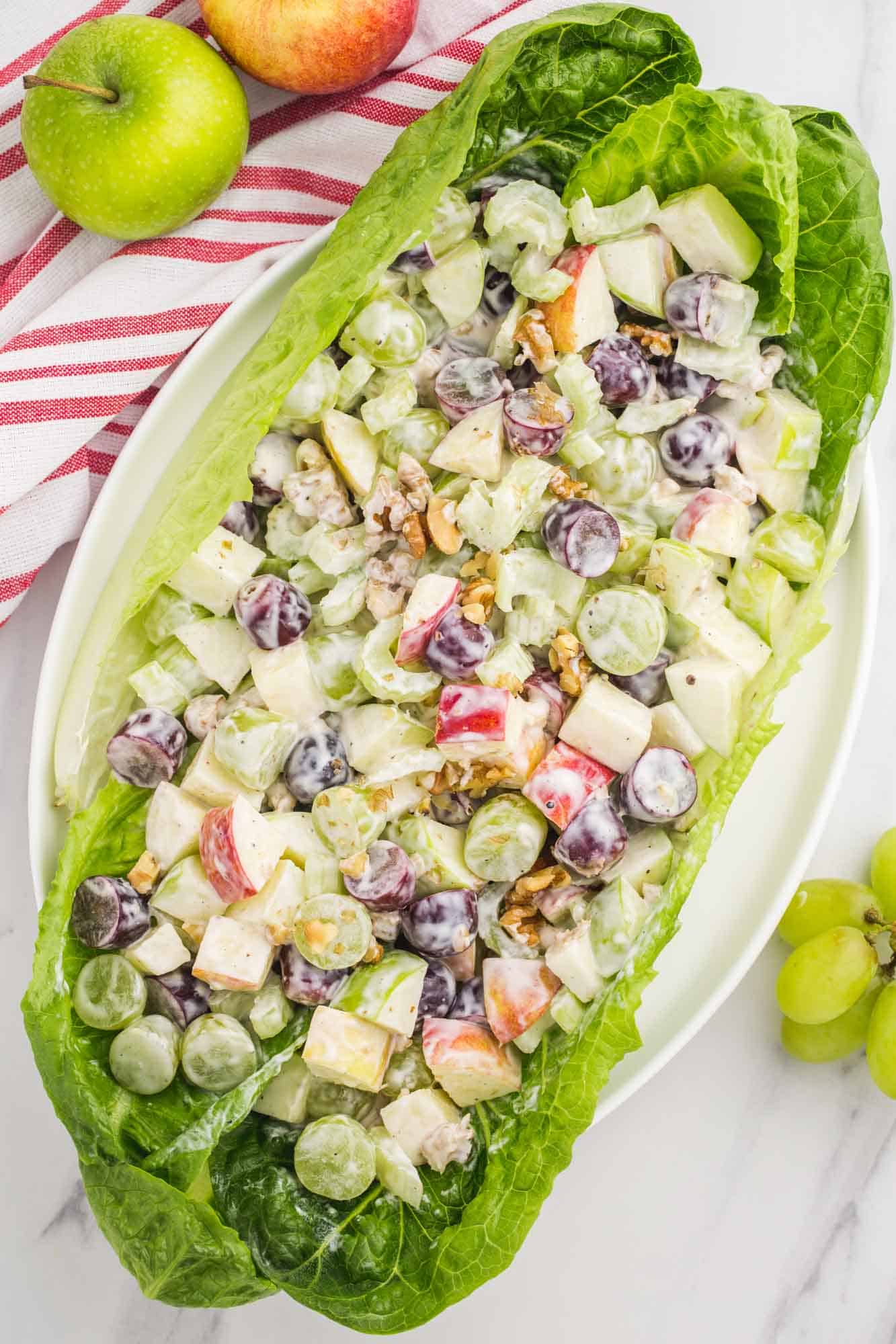 Waldorf salad filled lettuce leaf, viewed from above, surrounded by fruit.