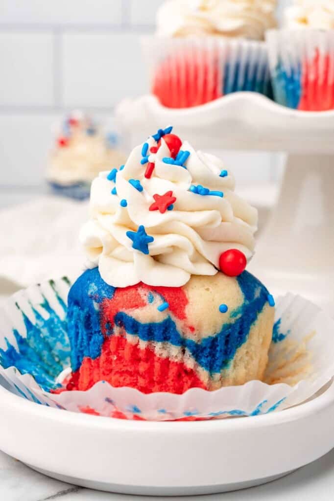 a red white and blue tie dye cupcake, unwrapped, on a small plate.