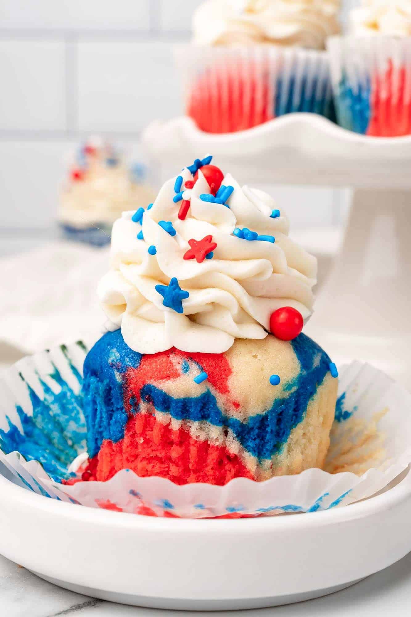 a red white and blue tie dye cupcake, unwrapped, on a small plate. 