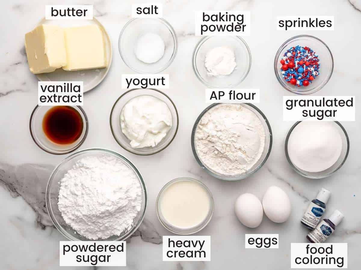 The ingredients for making fourth of july cupcakes, in separate bowls on a marble countertop. 