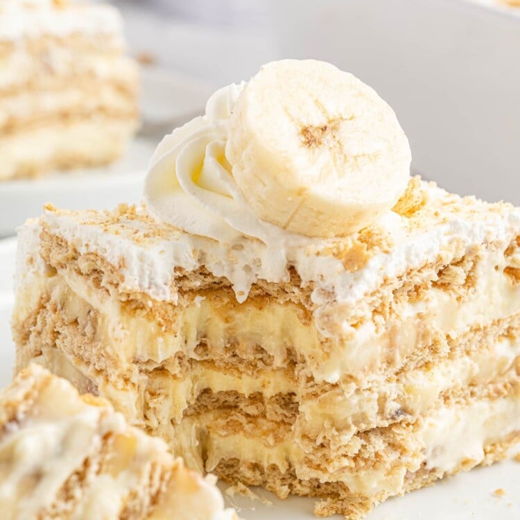 a square piece of graham cracker and banana pudding icebox cake with a bite taken off one corner