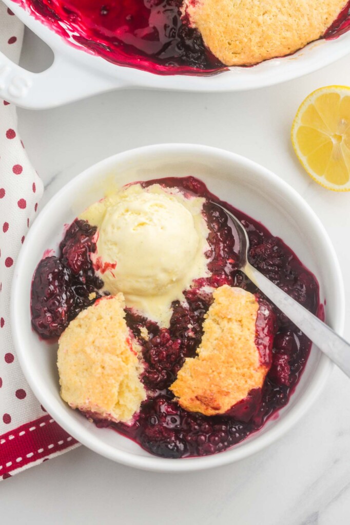 a serving of homemade blackberry cobbler in a white bowl with a scoop of ice cream on top, viewed from above