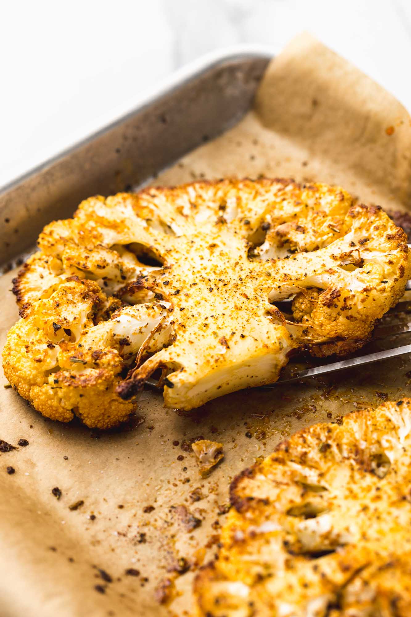 Taking a roasted cauliflower steak from the roasting pan