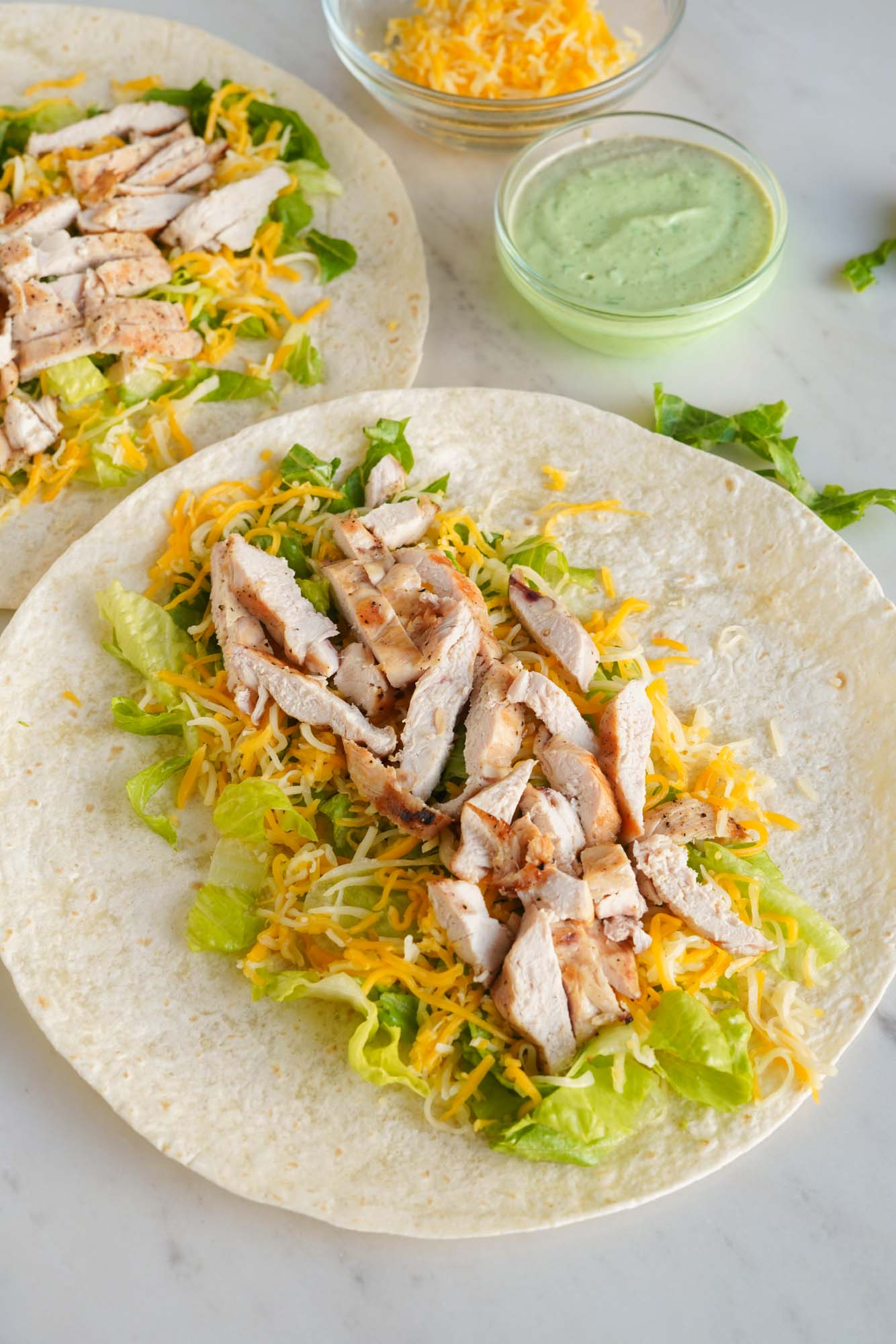 Two wraps filled with lettuce, cheese, and grilled chicken.