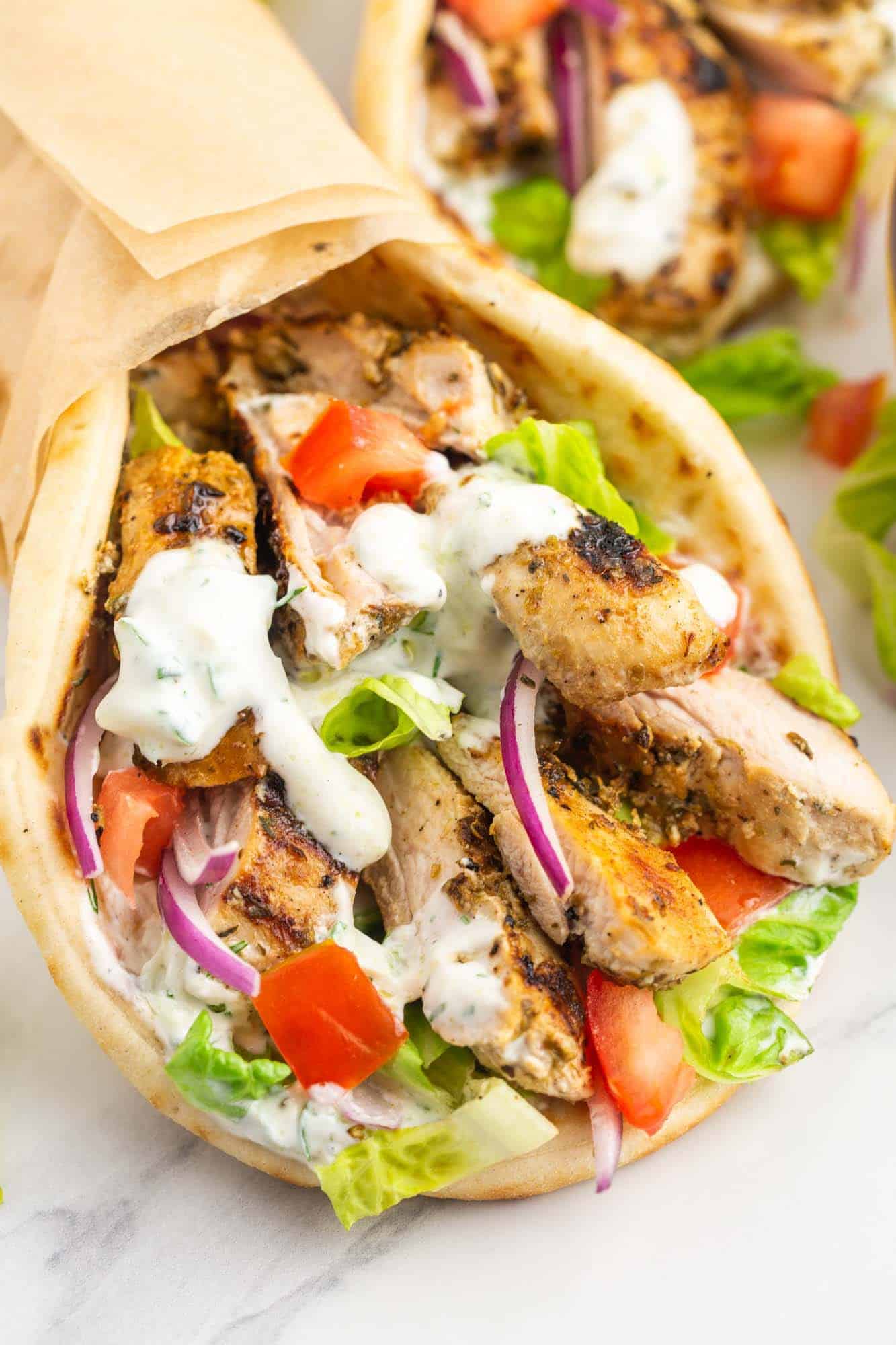 Close up shot of a chicken gyros wrap with extra tzatziki sauce, placed on a white marble surface