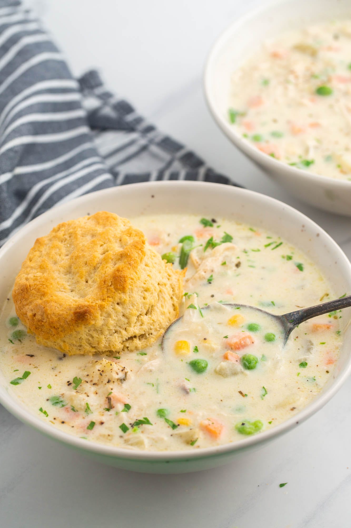 chicken pot pie soup in a white bowl, with a homemade biscuit and a spoon