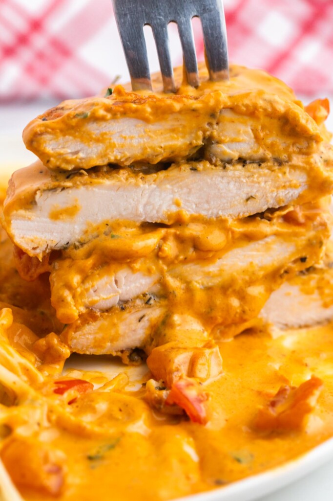 Chicken in tomato sauce on a plate, sliced. A fork is holding a stack of 4 slices of chicken.