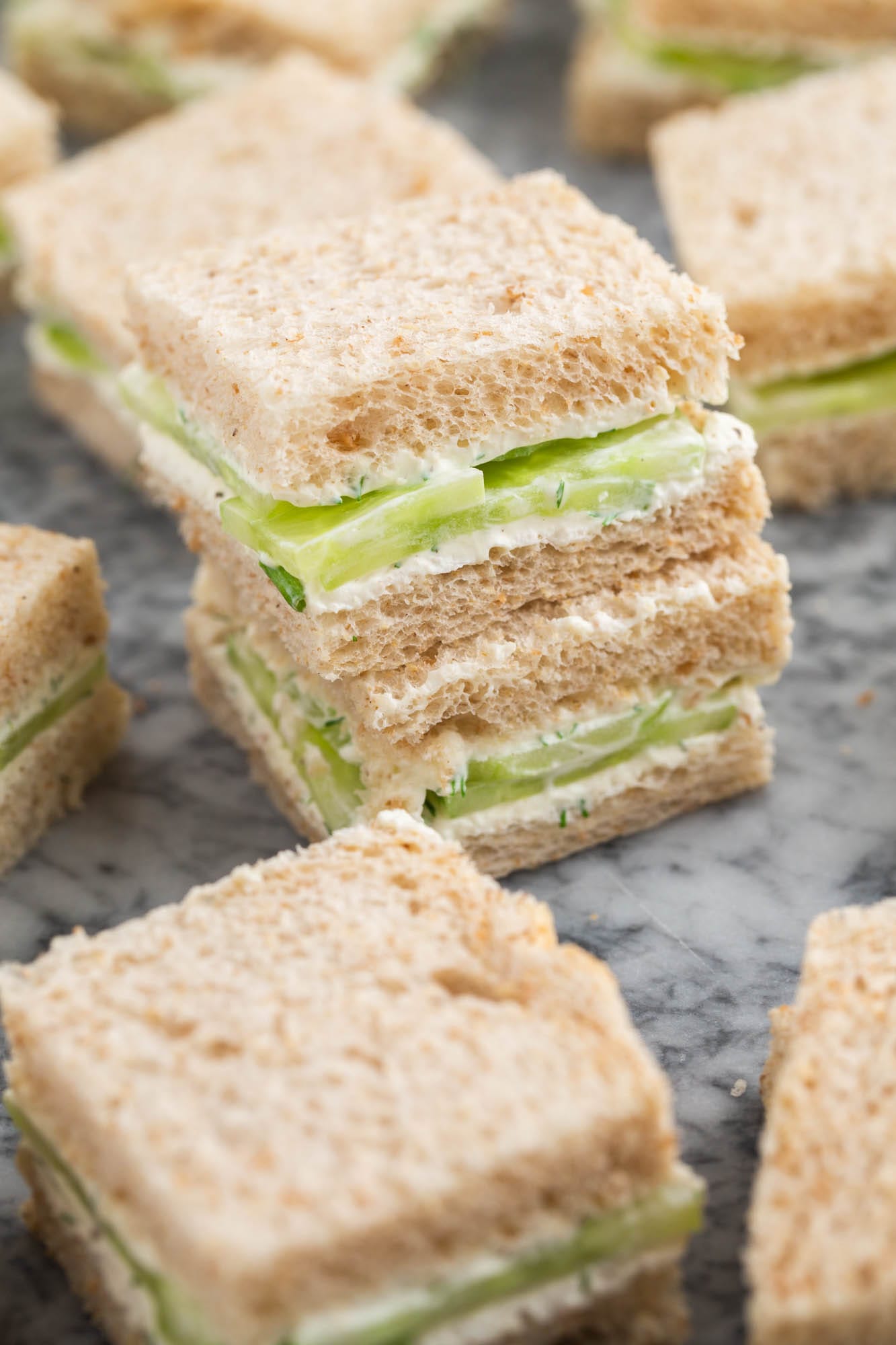 closeup of cucumber sandwiches cut into squares on a cutting board.