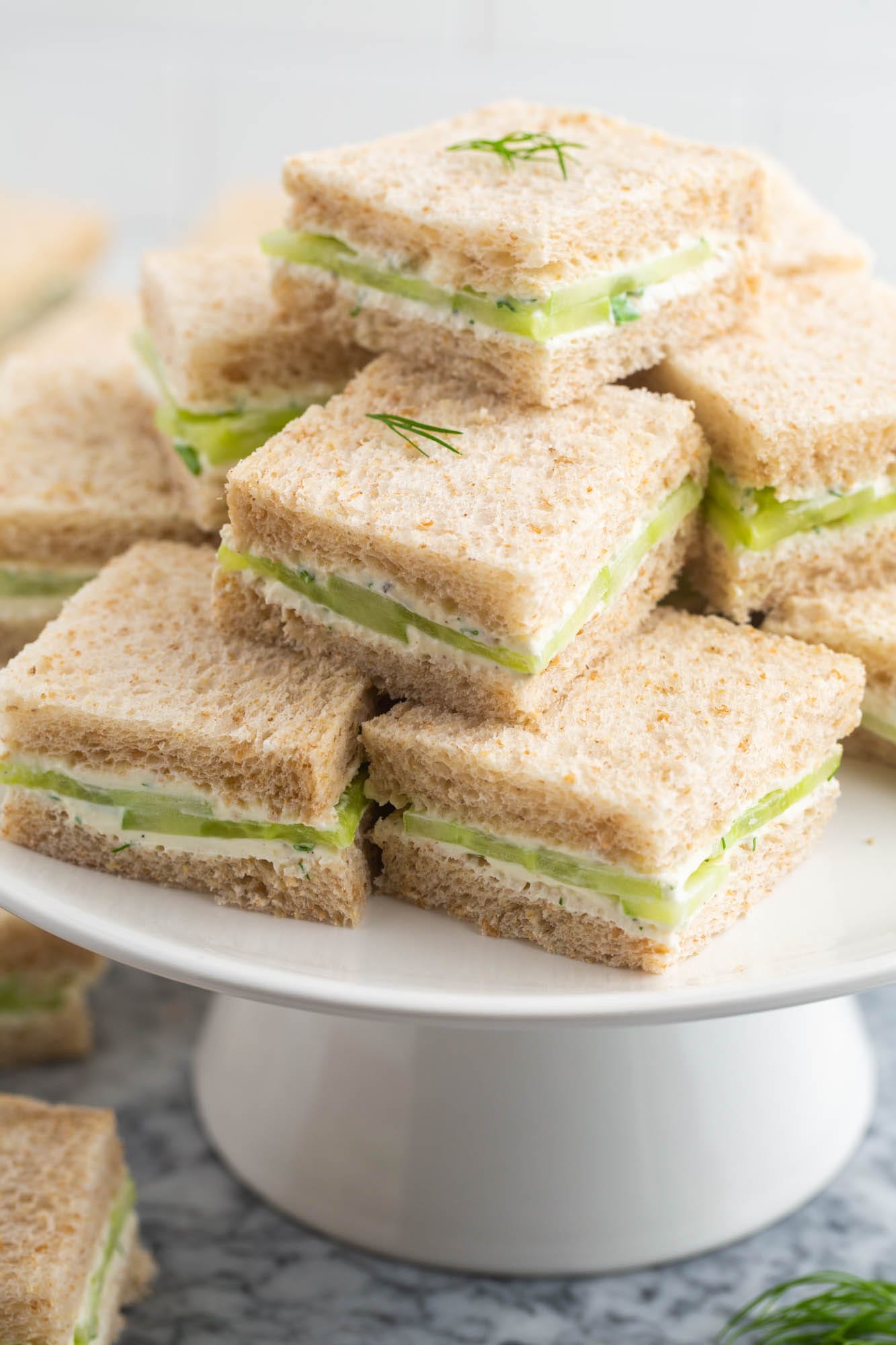 a cake pedestal filled with cucumber sandwiches