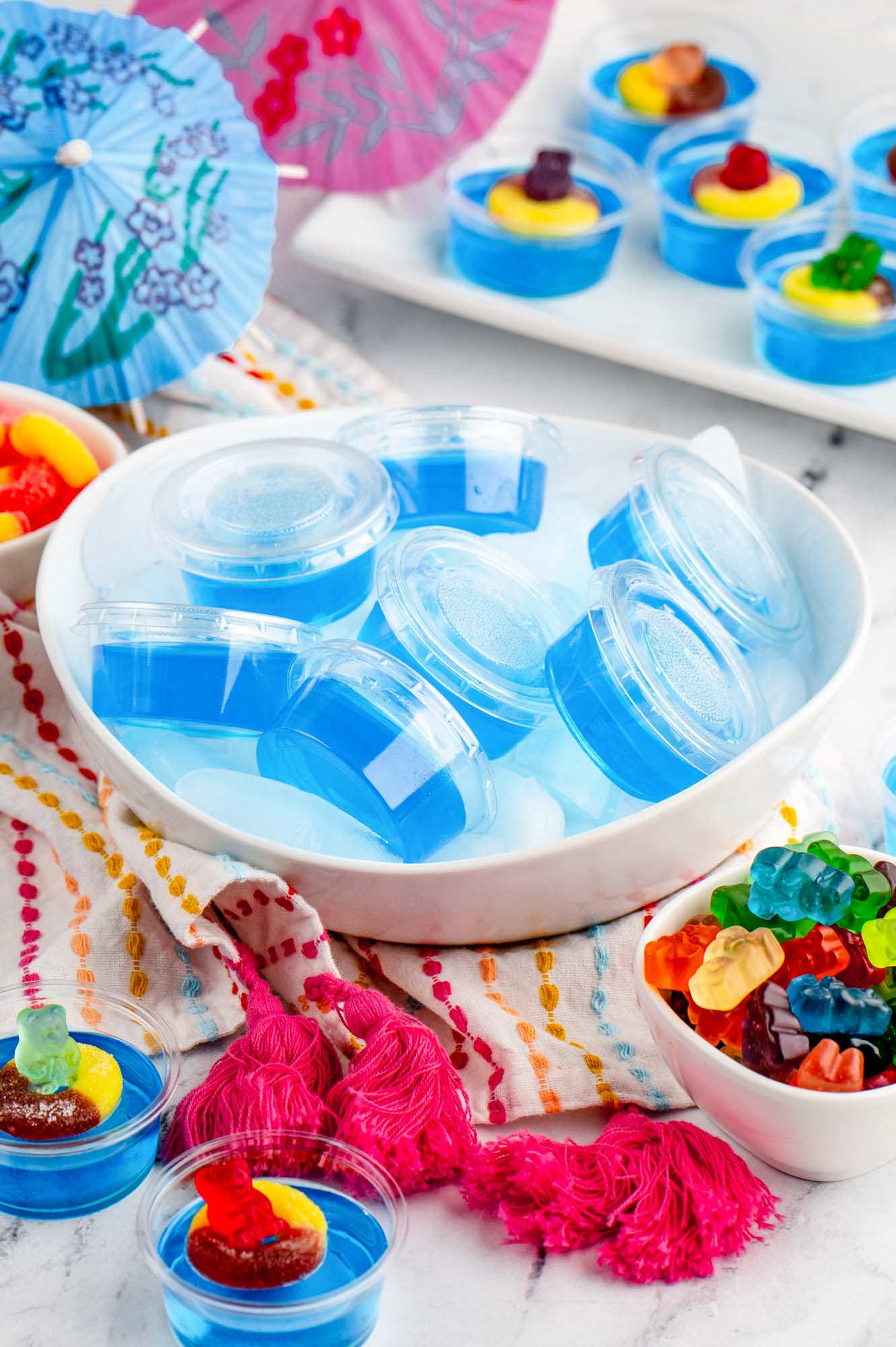 a bowl of blue jello shots with lids surrounded by gummy candies ready to decorate