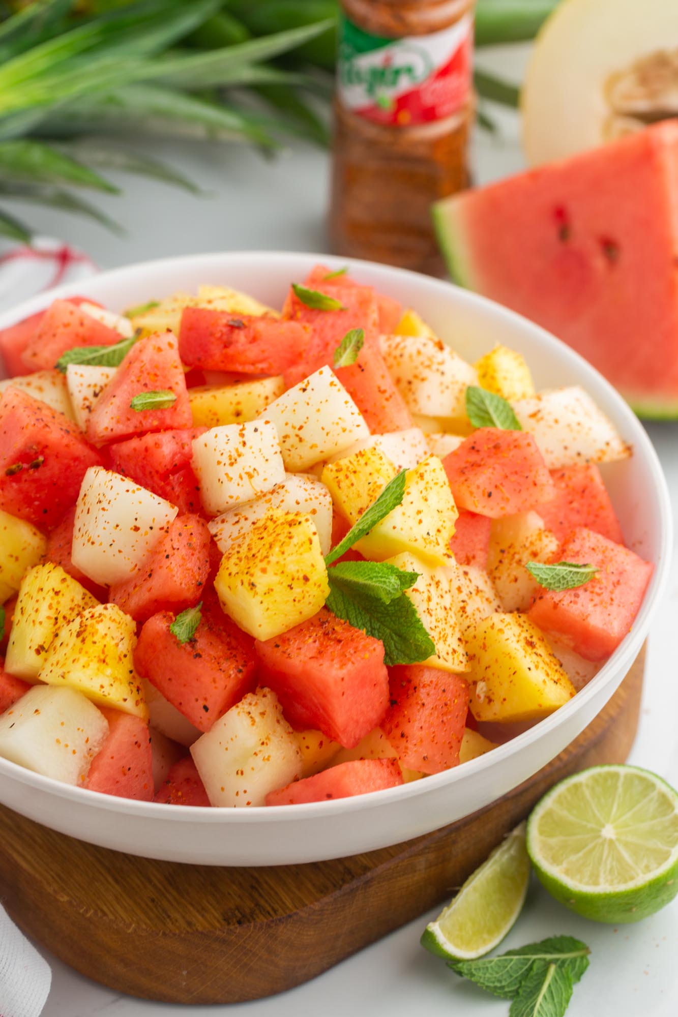 Mexican fruit salad in a bowl, with tajin in the background and lime