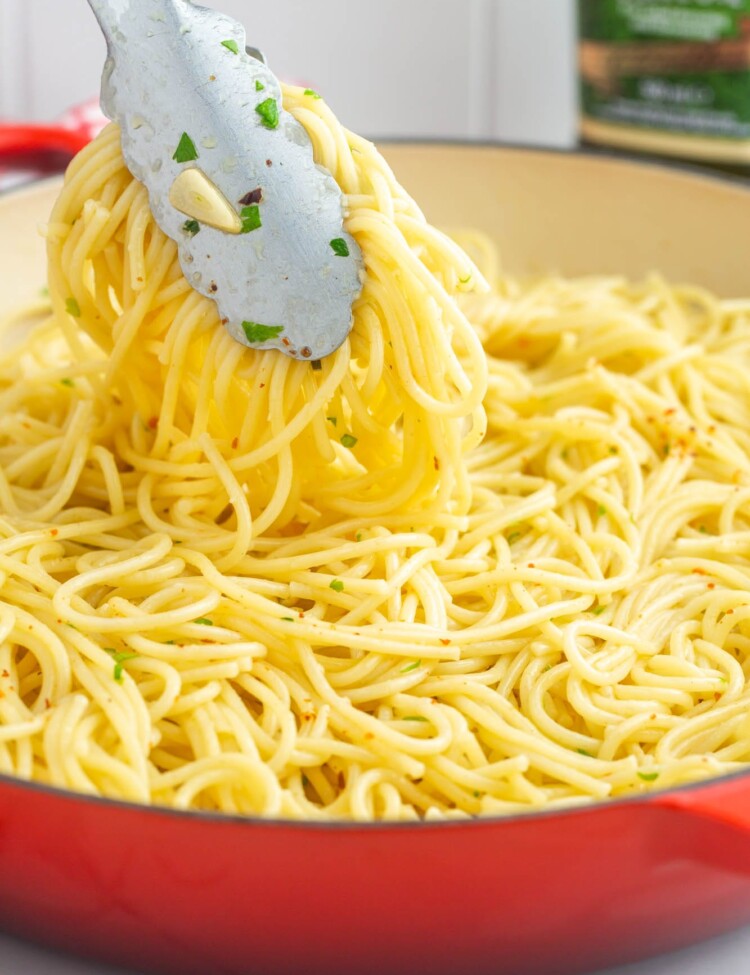 a red saute pan filled with spaghetti with olive oil and garlic