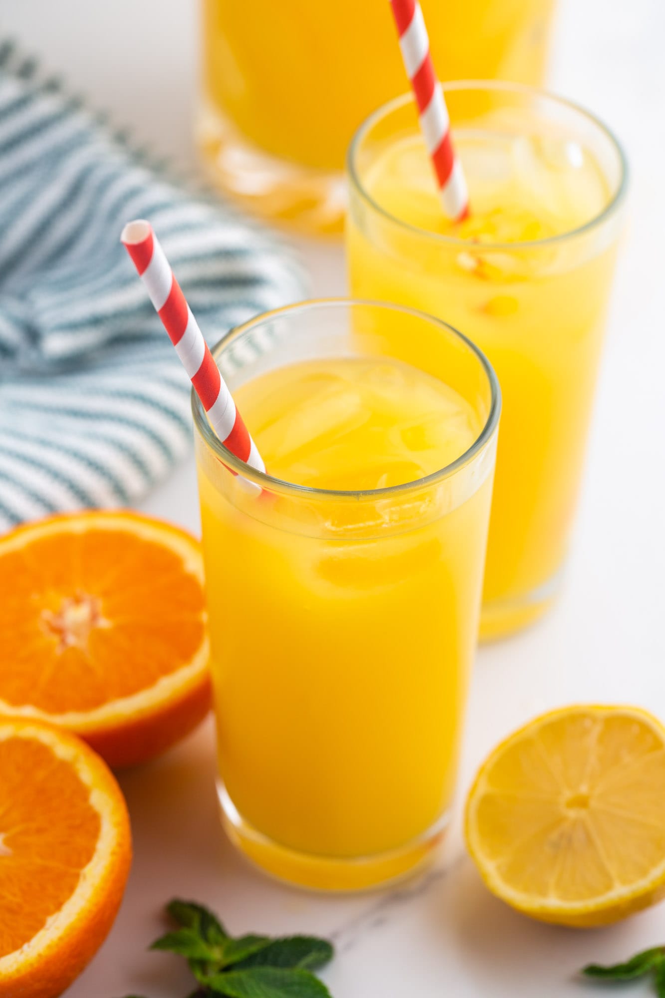 2 glasses of orangeade with straws, and sliced orange and lemon on the sides