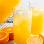 Pouring orangeade from a pitcher into a glass with ice cubes