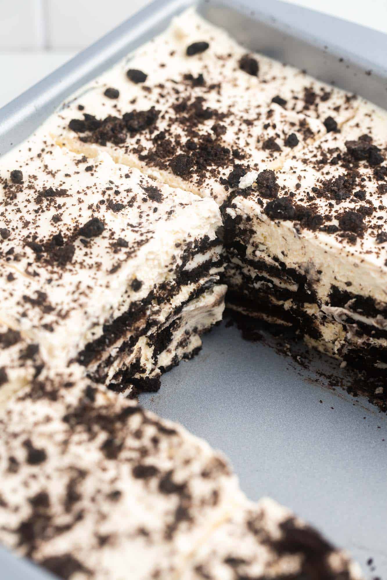 a pan of oreo icebox cake that has been cut into squares. Two pieces from the middle have been cleanly removed. 
