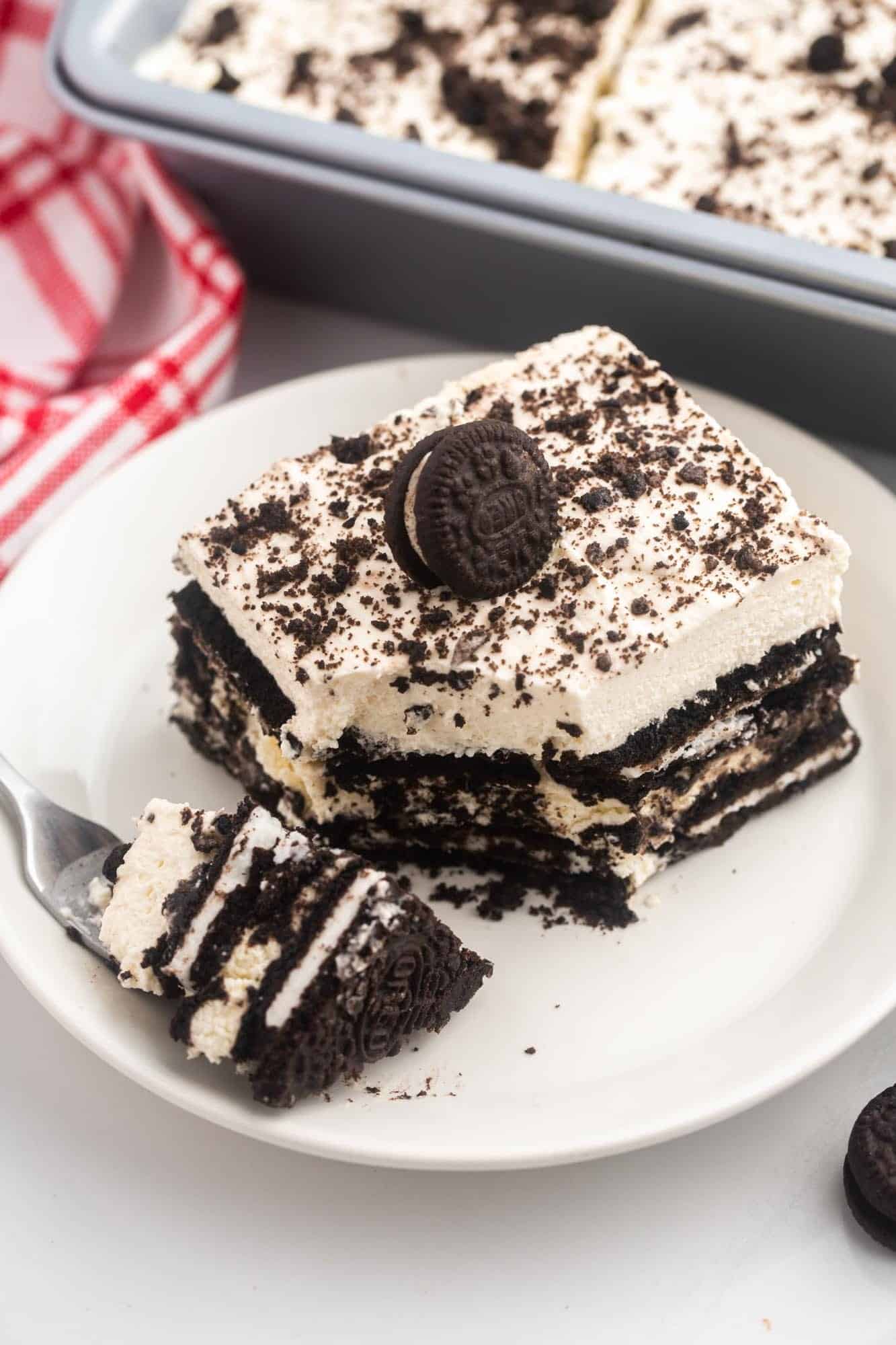 a square piece of Oreo icebox cake on a plate. A fork is on the side of the plate with a bite taken