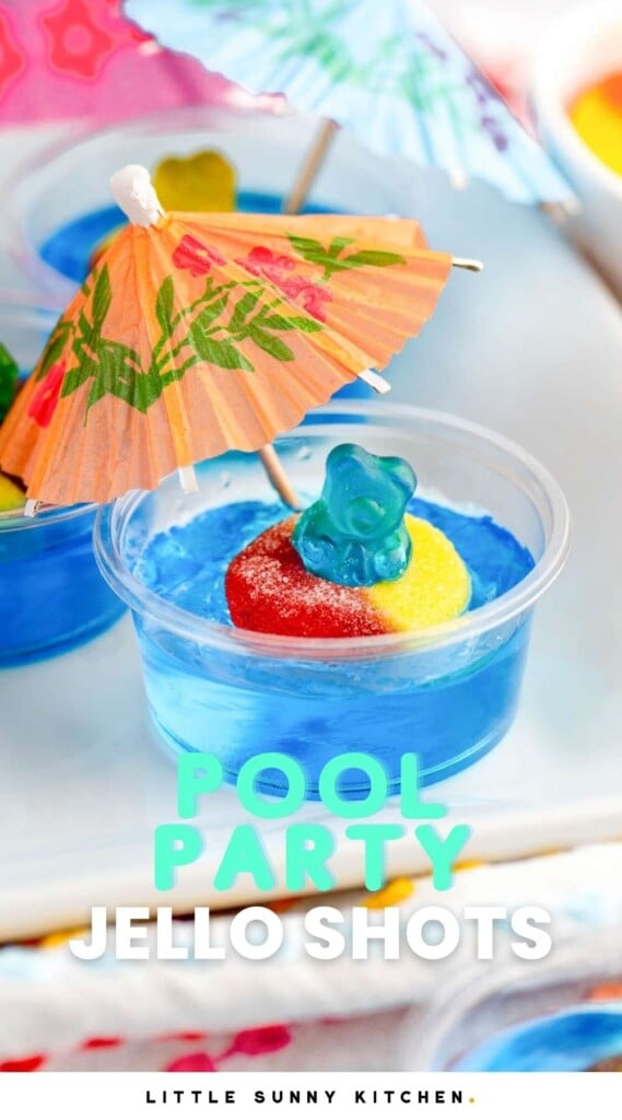 a blue jello shot with a blue gummy bear in a peach ring inner tube. A cocktail umbrella is stuck in the jello. text over image says Pool Party Jello Shots