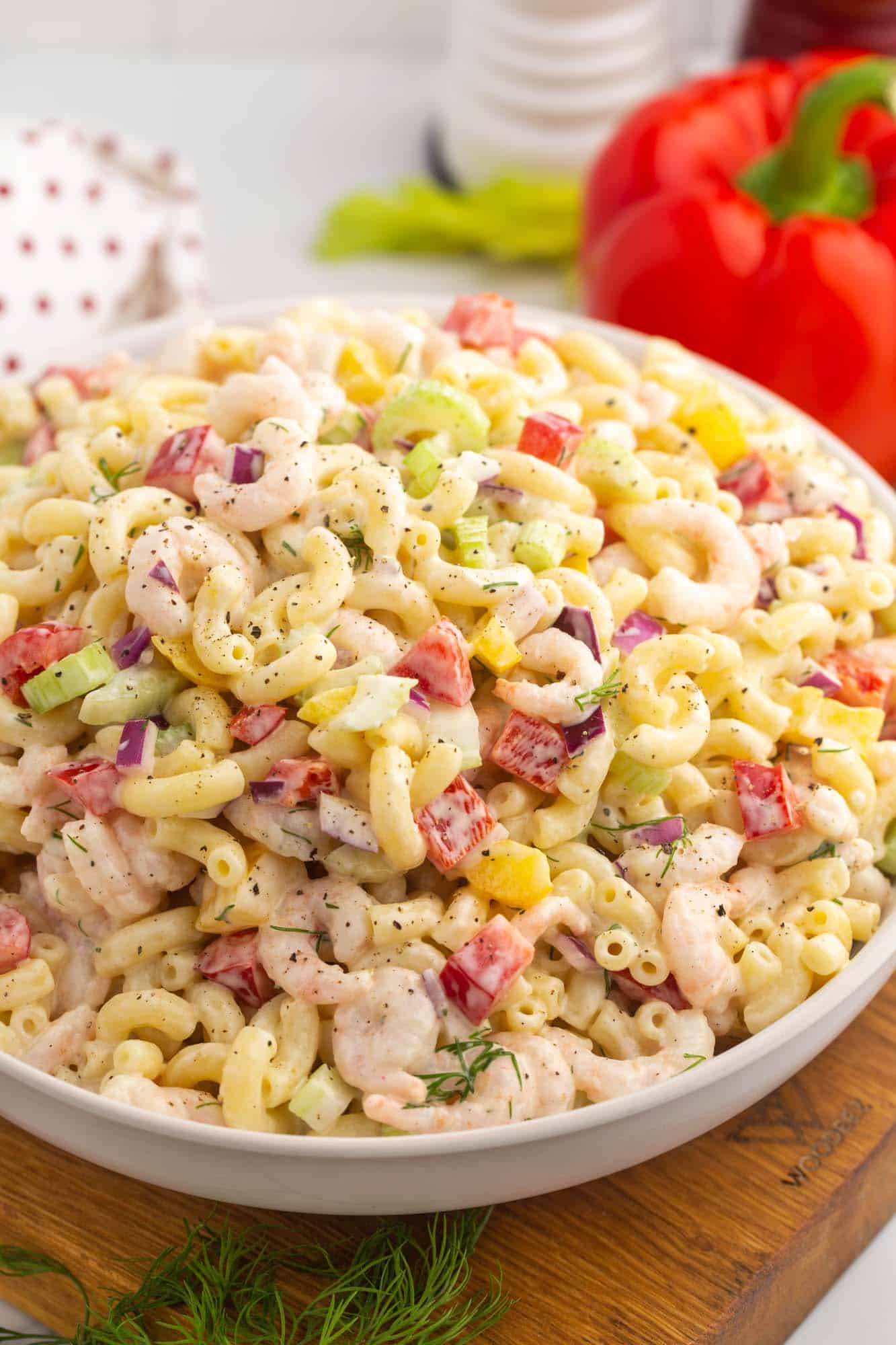 a large white bowl filled with shrimp macaroni salad with diced bell peppers