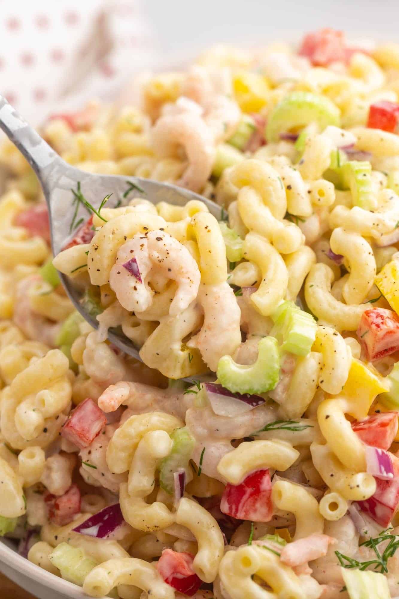 a closeup shot of a bowl of shrimp macaroni salad being served with a metal spoon