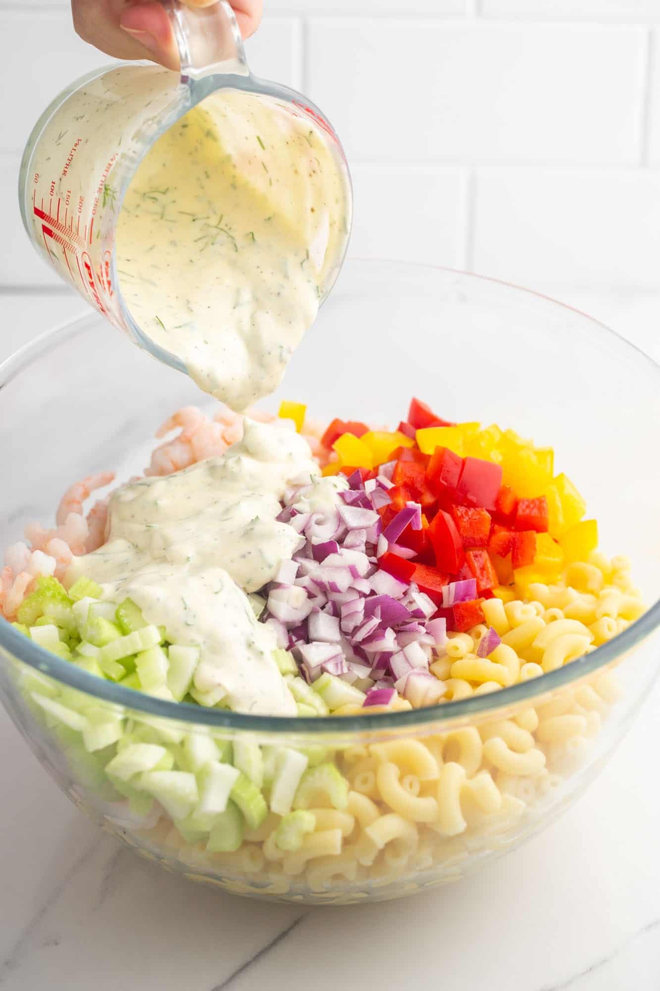 creamy dill dressing being poured over the rest of the shrimp salad ingredients