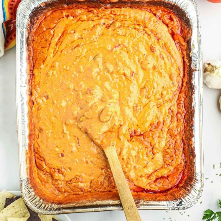 Overhead shot of smoked queso in a large foil pan, with a wooden spoon.