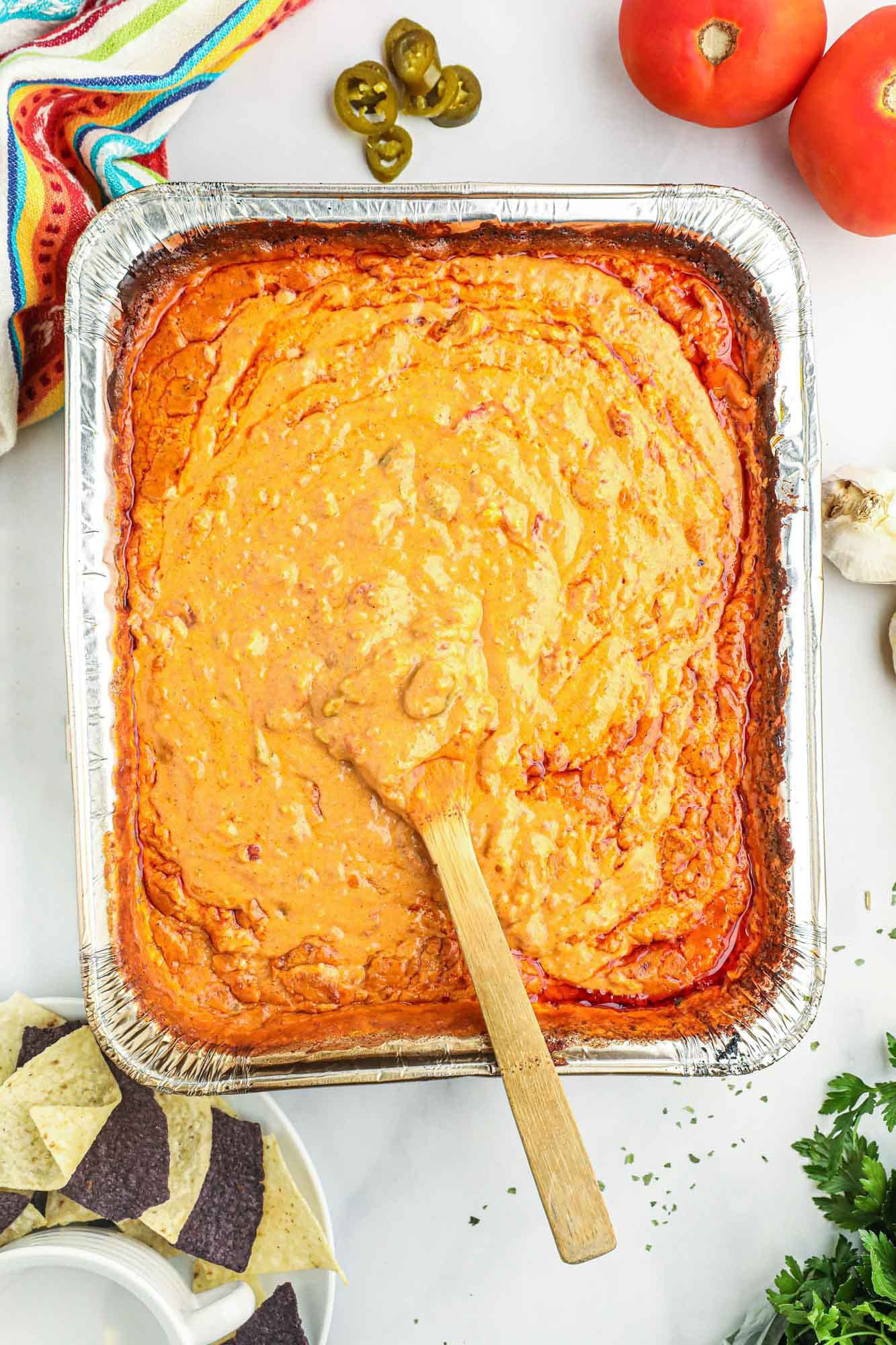 Overhead shot of smoked queso in a large foil pan, with a wooden spoon.