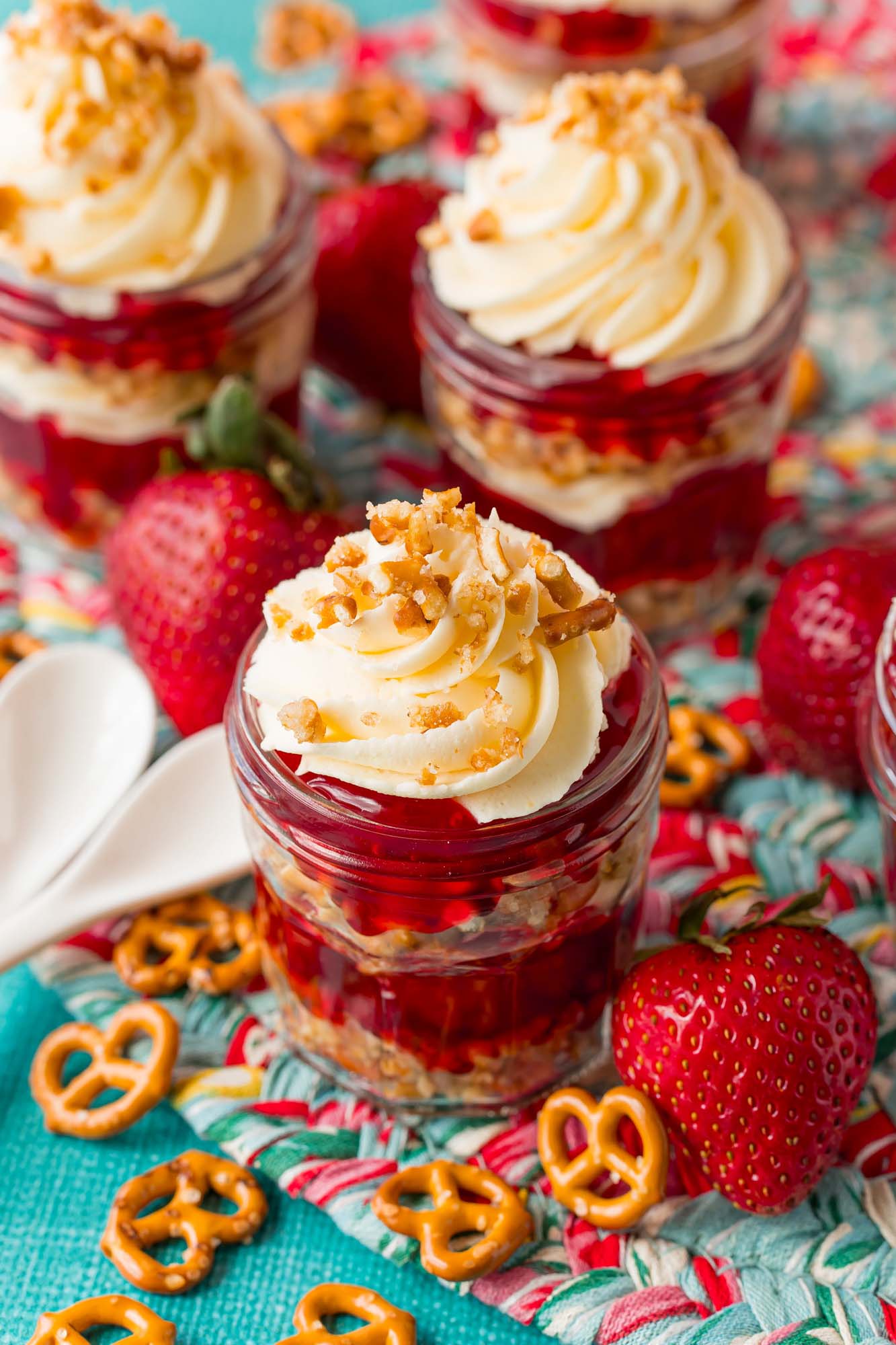 a batch of strawberry pretzel parfait on a blue counter with strawberries and tiny pretzels strewn about