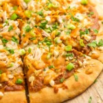 Sliced thai chicken pizza, garnished with sliced green onions, and roasted peanuts.