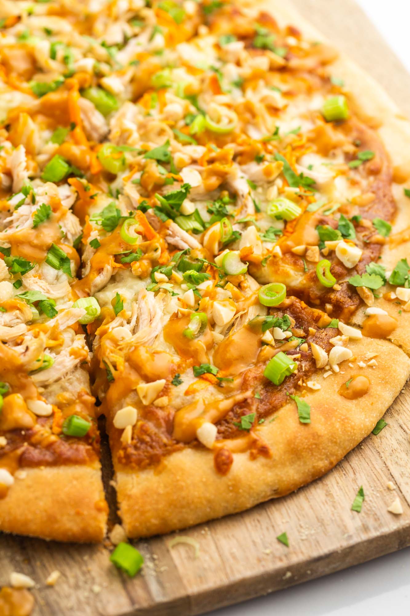 Sliced thai chicken pizza, garnished with sliced green onions, and roasted peanuts.