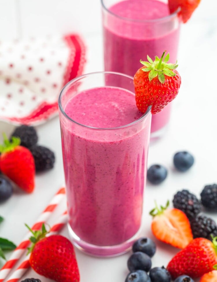 2 glasses with pink mixed berry smoothies, and fresh berries on the side.