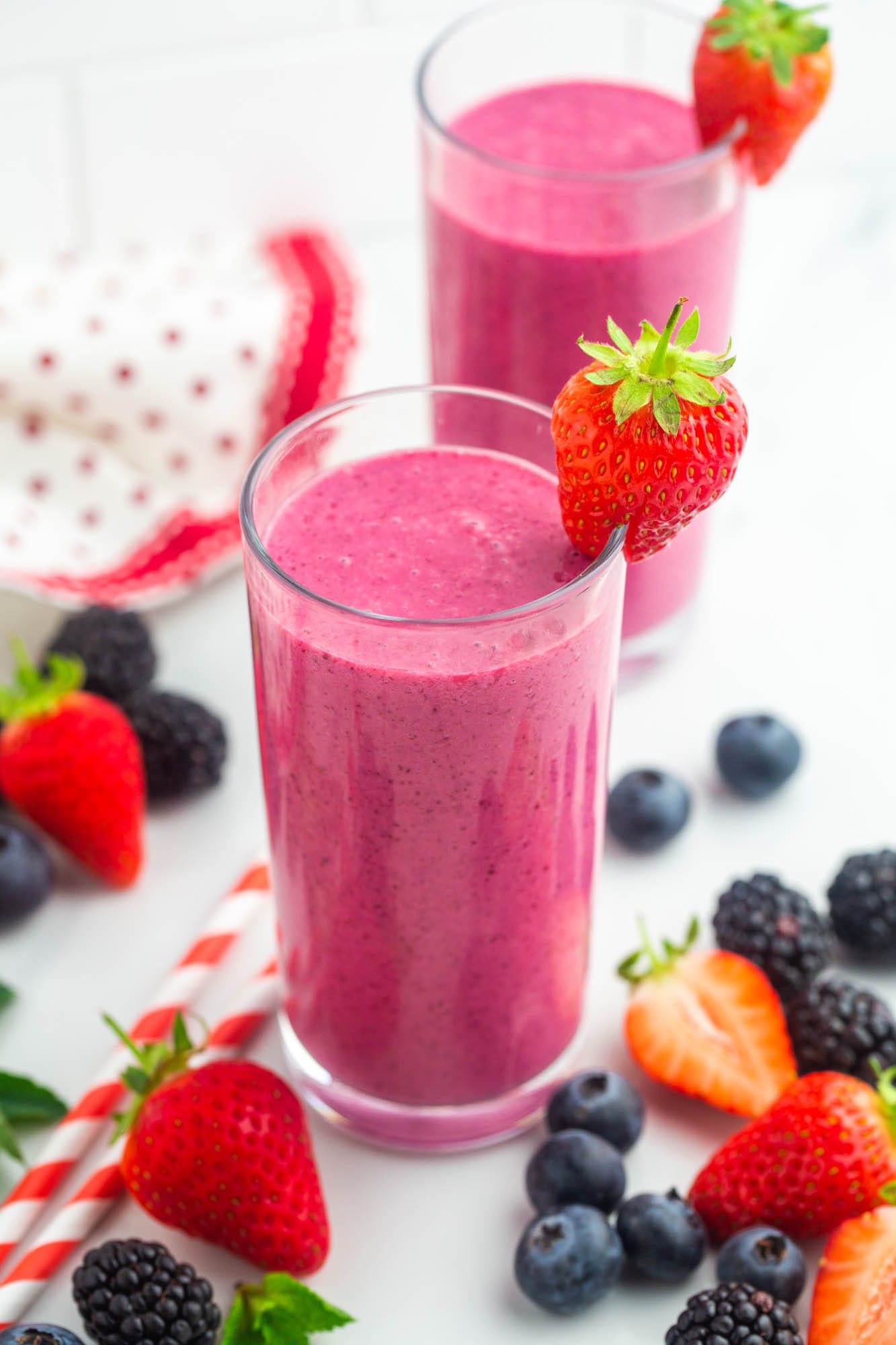 2 glasses with pink mixed berry smoothies, and fresh berries on the side.