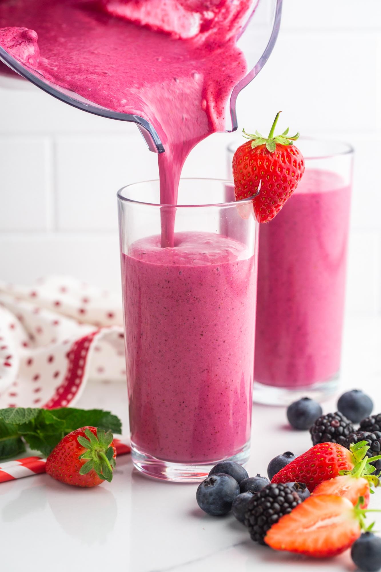 Pouring pink berry smoothie from a blender jug into a glass