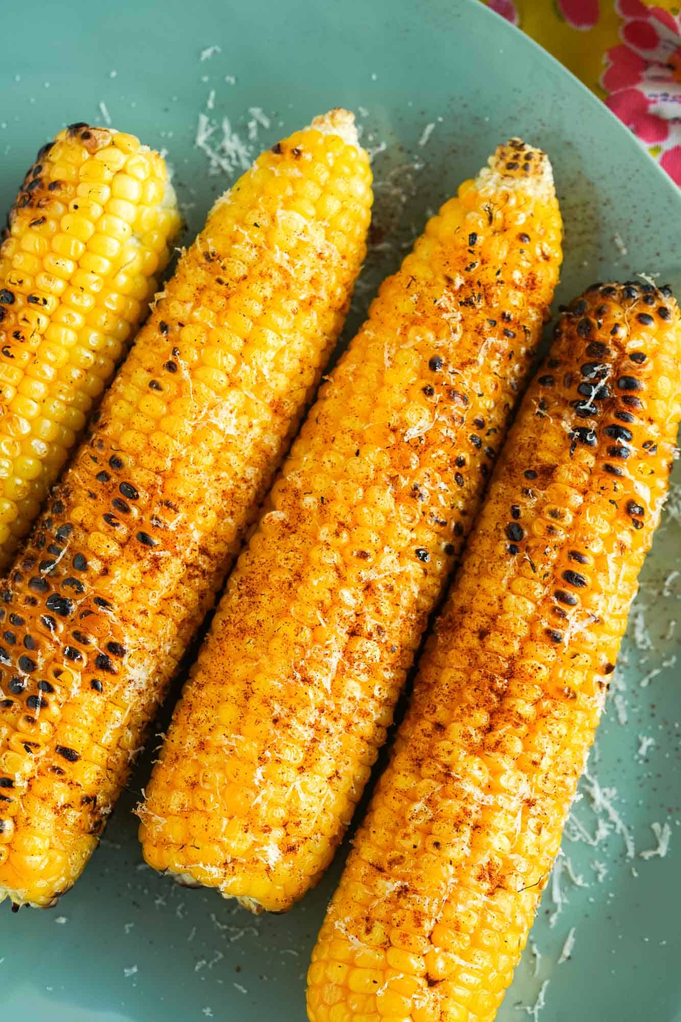 four ears of grilled corn on a green plate. 