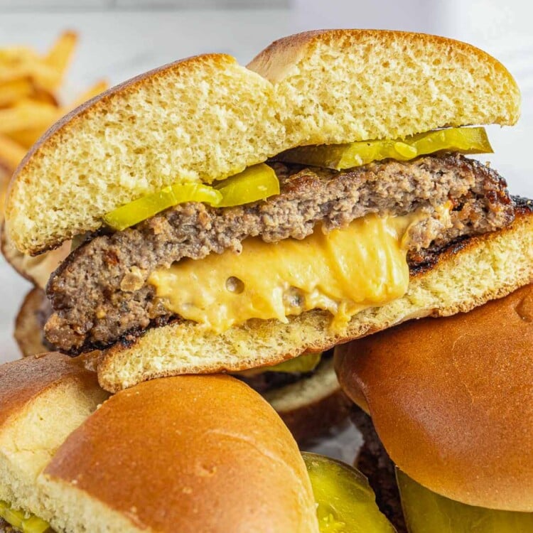 a juicy lucy hamburger on a bun stuffed with melty american cheese, sliced in half to show the texture.