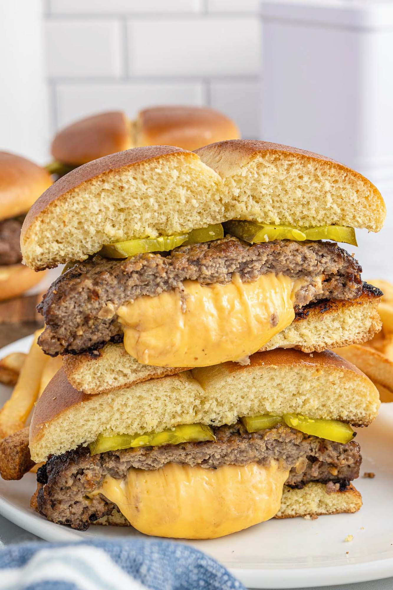 a cheese stuffed hamburger on a roll with pickles, cut in  half and stacked up on a plate. 