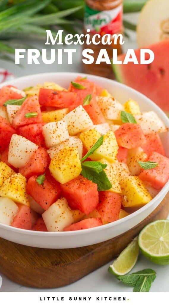 A bowl of Mexican fruit salad garnished with tajin, mint leaves, and lime. And overlay text that says "Mexican fruit salad"