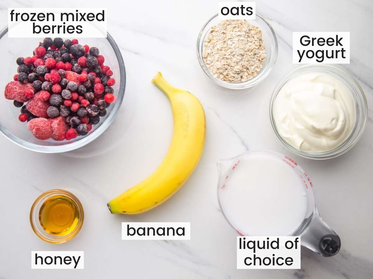 Ingredients needed for making a berry smoothie including frozen berries, banana, honey, oats, yogurt, and milk.