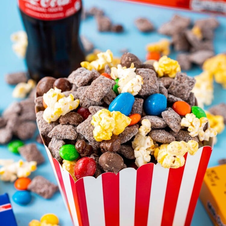 a red and white popcorn box filled with chocolate chex mix with popcorn and candy.