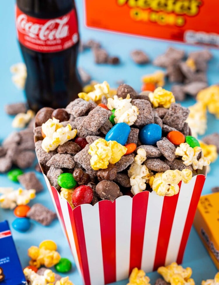 a red and white popcorn box filled with chocolate chex mix with popcorn and candy.