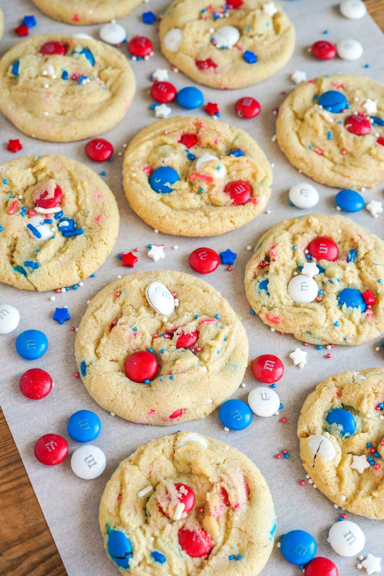 Angle shot of Red White And Blue M&M Cookies on white parchment paper, showing a bite shot. With patriotic M&M's and sprinkles scattered.